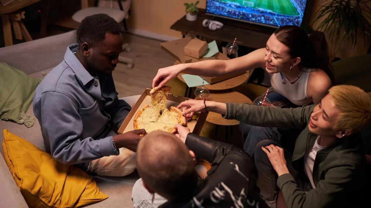 Amigos comiendo pizza mientras ven partido de fútbol - Getty Images Creative
